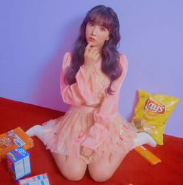 三上悠亜 from the 디에세오스타 jacket photoshoot. she is sitting cutely on the floor, surrounded by various colourful snacks.