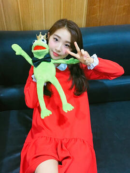 여진 smiling sweetly whilst holding up a kermit the frog puppet. kermit is dressed up in a gold crown and a bowtie.